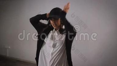 一位长头发的年轻女子，身穿白衬衫、黑裤子、夹克和黑帽子，跳着现代爵士乐